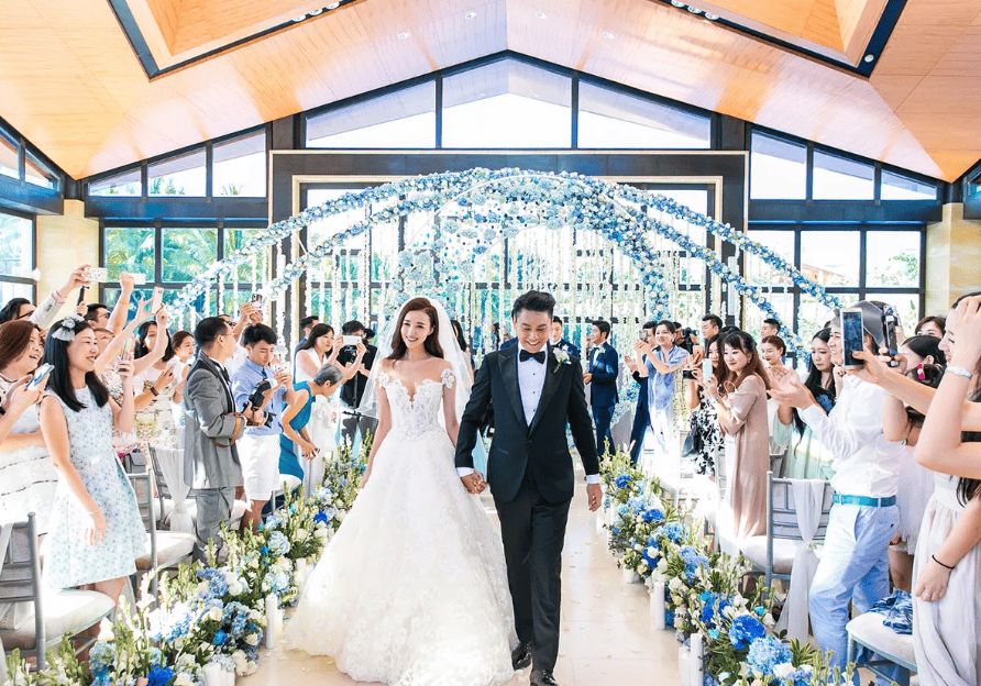 Ken Zhu and Vivian Han walking down the aisle at their Bali wedding with blue floral décor